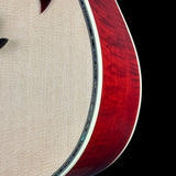 Close-up of an acoustic guitar body showing the red flamed maple wood side and the beige fabric-covered soundboard, set against a solid black background.