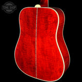 Close-up of the back of an acoustic guitar showing a vibrant red flamed wood finish with a white binding edge, set against a solid black background.