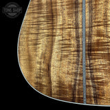 Close-up of an acoustic guitar body showing a rich wood grain finish with a decorative inlay running vertically down the center, set against a solid black background with a Tone Shop watermark in the top-left corner.