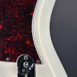 Close-up detail of an electric guitar showing the edge of a glossy red maple pickguard, a cream-colored body, and a chrome hardware component against a dark gray background.