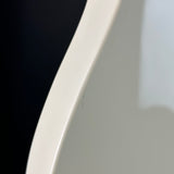 Close-up of a glossy white curved surface, likely part of a chair or furniture piece, with a dark black background visible on the left.