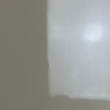 A close-up, slightly blurry view of a plain light gray or off-white surface with a soft gradient and a small dark vertical edge on the left.