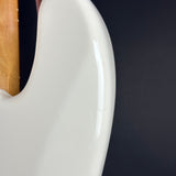 Close-up of the glossy white side body of an electric guitar, showing a small amount of the natural wood neck at the upper left against a dark background.