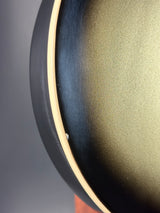 Close-up detail of a round product showing a dark charcoal exterior, a black rim, and a textured metallic gold interior surface.