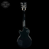 A black electric guitar shown from the back against a solid black background, with a Tone Shop logo watermark in the top-left corner.