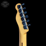 Close-up of the headstock of an electric guitar with a natural wood finish and dark blue tuning pegs, shown against a solid black background with a Tone Shop watermark in the top left corner.