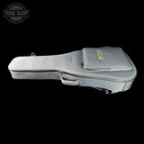 A gray padded guitar case with a zippered top pocket and a small gold logo, shown against a solid black background. A Tone Shop watermark is visible in the upper left corner.