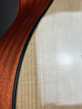 Close-up detail of an acoustic guitar body showing the flamed maple top and the rich reddish-brown wood grain of the sides, separated by a black binding edge.
