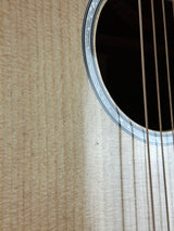 Close-up detail of an acoustic guitar body showing the sound hole, rosette, strings, and light natural wood grain.