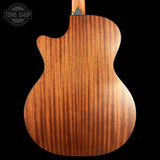 Close-up of the back of an acoustic guitar showing a rich, figured wood grain finish in warm brown tones against a solid black background. A Tone Shop watermark is visible in the top-left corner.