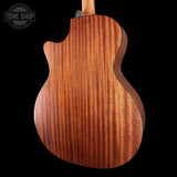 Close-up of the back of a wooden acoustic guitar showing a rich wavy grain pattern in warm brown tones, set against a solid black background with a Tone Shop watermark in the top left.
