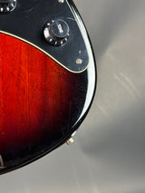 Close-up of a guitar headstock with a wooden finish and control knobs on a gray background