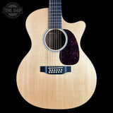 A light natural wood cutaway acoustic guitar shown from the front against a solid black background, with a Tone Shop watermark in the upper left corner.