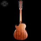 The back view of a wooden acoustic guitar with a cutaway body and six tuning pegs, shown against a solid black background with a Tone Shop watermark in the top-left corner.
