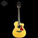 A Taylor acoustic-electric guitar with a natural wood finish and a red pickguard, shown against a solid black background with a Tone Shop watermark in the top left corner.