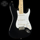 A black electric guitar with a white pickguard and a light maple neck, shown against a solid black background. A Tone Shop logo is visible in the top-left corner.