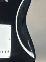 Close-up of a glossy black electric guitar body with a white pickguard and visible wear scratches on the upper bout area.
