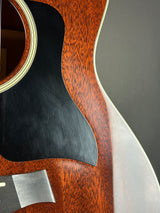 Close-up detail of an acoustic guitar body showing the reddish-brown wood grain, a black pickguard, and part of the soundhole rim.