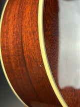 Close-up detail of an acoustic guitar's wooden body, showing the rich reddish-brown wood grain and a light cream binding edge.