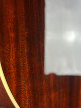 Close-up detail of a polished wooden acoustic guitar body showing the rich reddish-brown wood grain and a light cream binding edge.