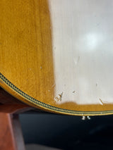 Close-up detail of a wooden instrument body, showing a light natural wood top, a gold-toned edge, and a dark decorative inlay.