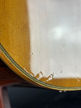 Close-up of a glossy wooden surface with visible scratches and wear, showing part of a curved edge with a decorative black and gold pattern.