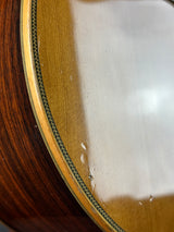 Close-up detail of an acoustic guitar's wooden body, showing the glossy light wood top, a decorative inlay, and the dark brown wood grain of the lower section.
