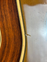 Close-up detail of an acoustic guitar body showing the wood grain, soundhole rosette, and a small hair-like defect on the glossy top.