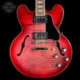 Red electric guitar with a black pickguard on a black background, featuring the Tone Shop logo.