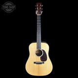 A natural wood acoustic guitar with a dark fretboard and headstock, shown against a solid black background. A circular 'TONE SHOP' watermark is visible in the top-left corner.