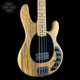 A natural wood five-string bass guitar with a black pickguard and control plate, shown against a solid black background with a Tone Shop watermark in the top left corner.