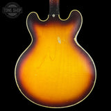 Close-up of the back of a classic electric guitar body, showing a sunburst finish that transitions from bright yellow-orange in the center to dark brown and black at the edges, with a gold-toned binding. A Tone Shop watermark is visible in the top left corner.