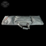 A dark gray padded instrument case, likely for a guitar or bass, shown horizontally against a solid black background. The case features a top zippered pocket, a carrying strap, and a small red brand patch on the left side.