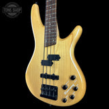 Electric bass guitar with a natural wood finish on a black background, featuring the Tone Shop logo.
