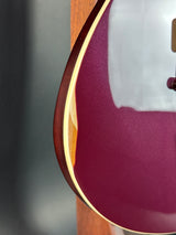 Close-up of a guitar body showing a glossy deep burgundy finish, a light cream binding edge, and part of the wooden neck behind it.