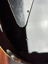 Close-up detail of a glossy dark brown electric guitar body, showing part of the pickguard, control hole, and a small section of the gold edge stripe.