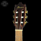 Close-up of the headstock of an Ibanez classical guitar against a solid black background, showing the dark brown wood, gold lettering, and tuning pegs.