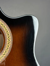Close-up of an acoustic guitar body showing the glossy sunburst finish, soundhole rosette, and edge contour against a neutral gray background.