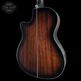 Close-up of the back of an acoustic guitar showing a rich dark brown wood grain finish, silver metal edge trim, and a gold tuning peg, set against a solid black background with a Tone Shop watermark in the top left.