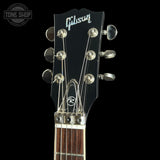 Close-up of a Gibson acoustic guitar headstock with six silver tuning pegs and strings, set against a solid black background.