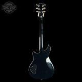 A black electric guitar shown from the back, featuring a glossy finish and chrome tuning pegs, set against a solid black background with a Tone Shop watermark in the top left corner.