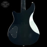 The rear view of a black electric guitar body, featuring a glossy finish, a silver pickguard, and a white binding edge, shown against a solid black background.