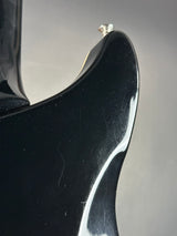 Close-up detail of a glossy black electric guitar body showing the edge of the neck joint and a small silver tuning peg against a neutral gray background.