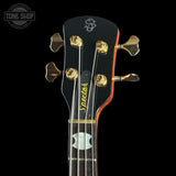 Close-up of a Spector bass guitar headstock with gold tuning pegs, a black finish, and an orange edge, shown against a black background.