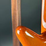 Close-up detail of a glossy orange-brown wooden instrument body corner with a visible wood neck behind it against a dark gray background.