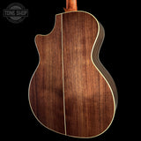Close-up of the back of an acoustic guitar with a rich dark brown wood grain finish and a single light-colored binding edge, shown against a solid black background with a Tone Shop watermark in the top left.