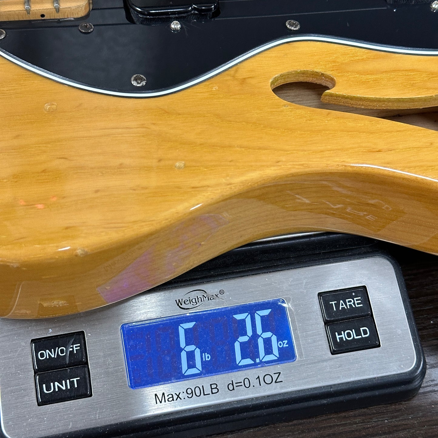 Wooden guitar body on a digital scale displaying weight