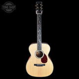 A natural wood acoustic guitar with floral inlays on the fretboard, shown against a solid black background with a Tone Shop watermark in the top left corner.
