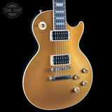 A gold-finish electric guitar with chrome hardware, dual humbucker pickups, and a black pickguard, shown against a solid black background with a Tone Shop watermark in the top left corner.