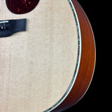 Close-up detail of an acoustic guitar body showing the natural wood soundboard, a portion of the dark brown fingerboard, and a decorative inlay along the edge against a black background.